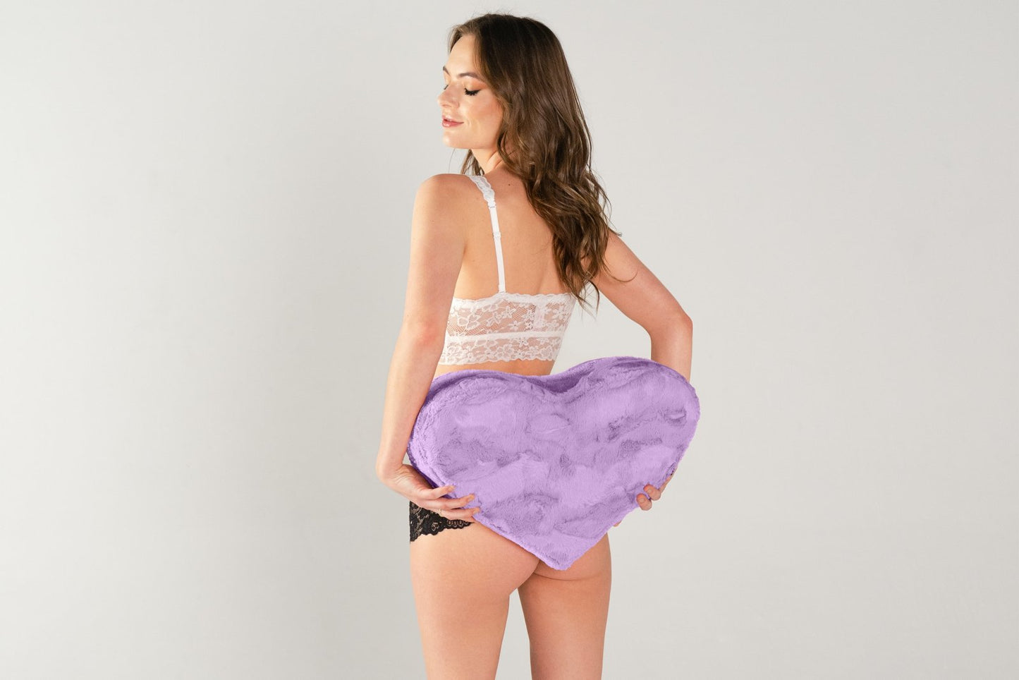 A person holds the Liberator Heart Wedge in Faux Fur behind their body, next to the butt. The Wedge looks wider than their small body | Kinkly