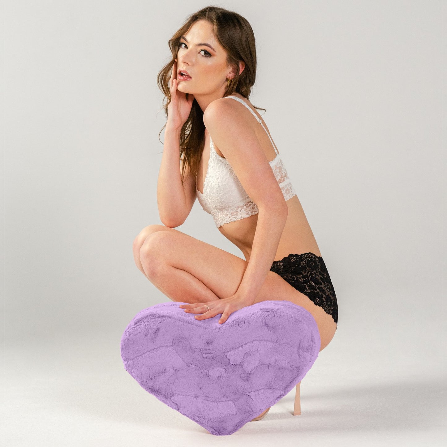 A person squats next to the Liberator Heart Wedge in Faux Fur in purple. They're pushing down on the shape, but the shape holds its shape under the pressure with the high-density foam design. | Kinkly