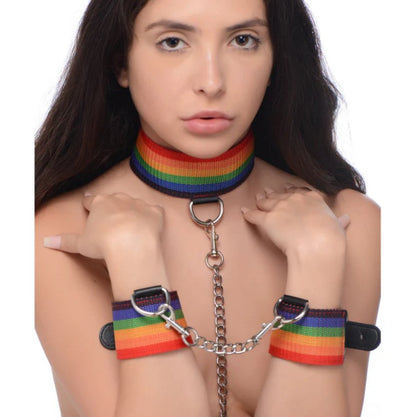 A person wears the Master Series Kinky Pride Rainbow Bondage Set collar and the wrist restraints. All three items are fastened to each other. | Kinkly Shop