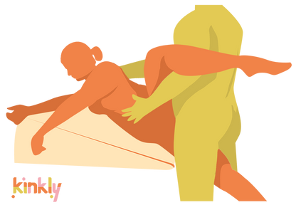 An illustrated sex position. It shows the Liberator Ramp pulled up to the edge of a bed. The receiving partner is laying, on their side, along the length of it. Their leg is in the air. The penetrating partner straddles their lower leg while getting close for penetration. | Kinkly Shop