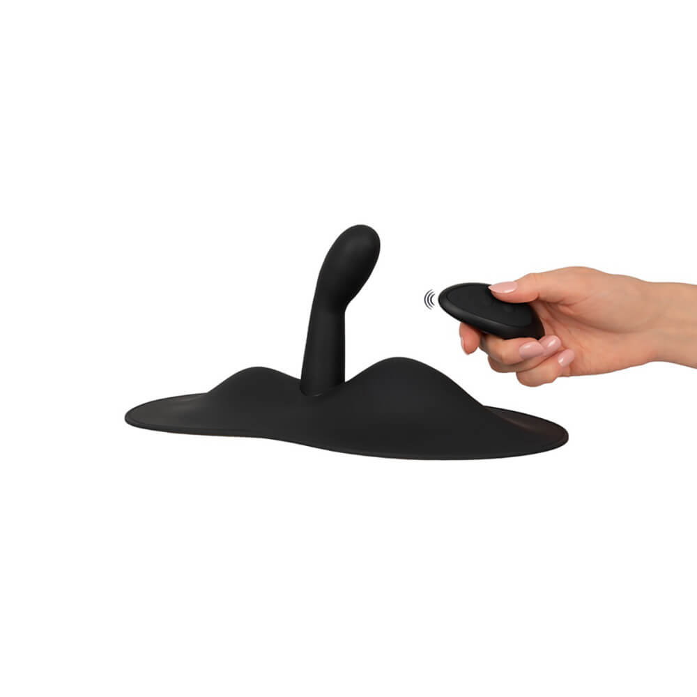 The Orion VibePad 3 sits on a white surface. A hand is holding the remote, clicking a button, to showcase the remote control capabilities of the Orion VibePad 3. | Kinkly Shop