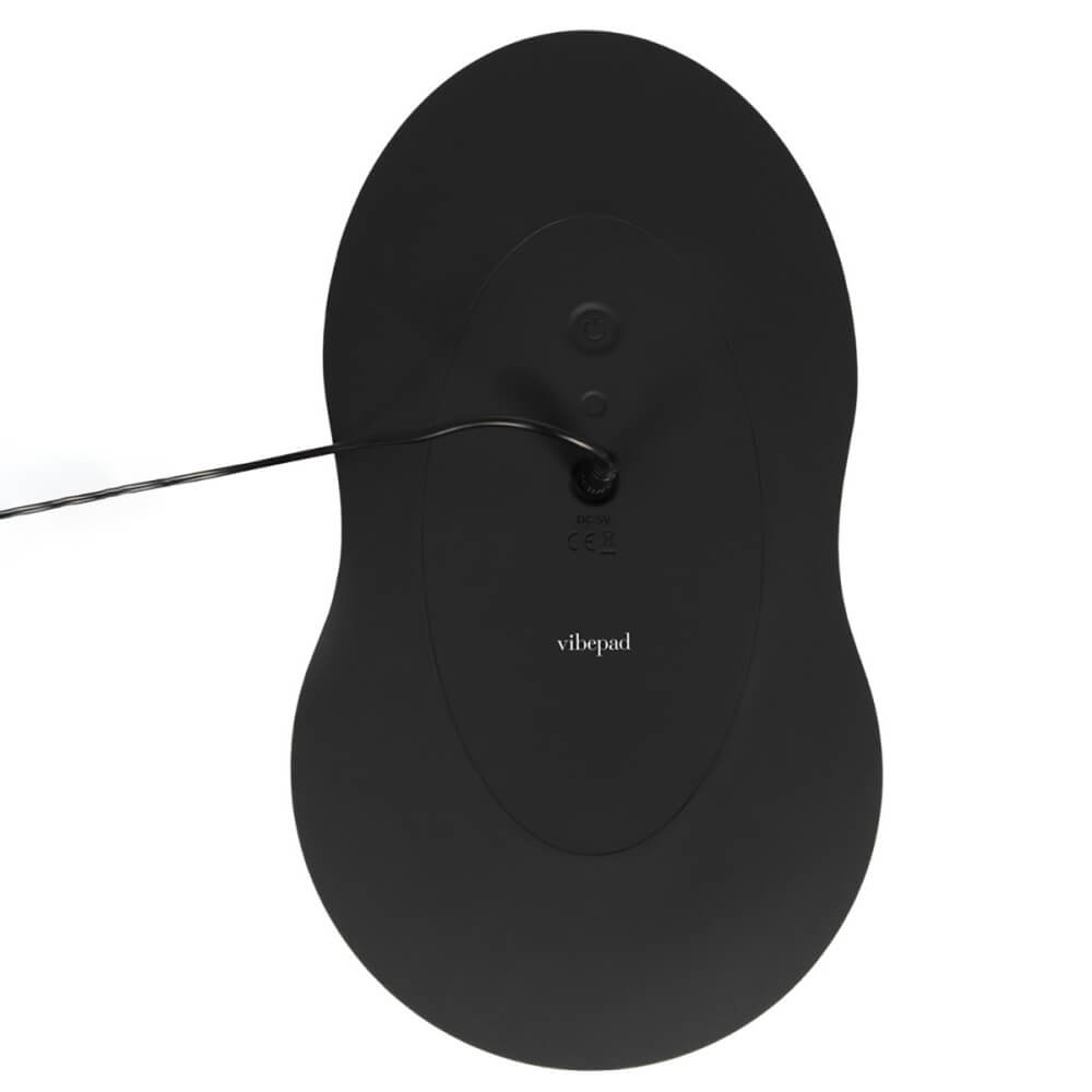 The Orion VibePad 3 is flipped upside down, showcasing the button and the charging port located underneath the toy. A charging cord is currently plugged into the VibePad to charge it. | Kinkly Shop
