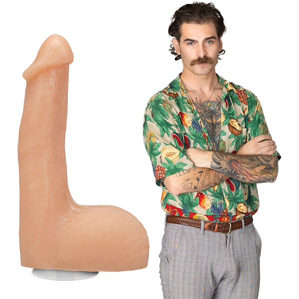 The Flesh Mechanic porn star stands fully clothed in 70's clothing with a bulge in their pants. The Signature Cocks - The Flesh Mechanic dildo is shown next to them, lifecast after their own shaft. | Kinkly Shop
