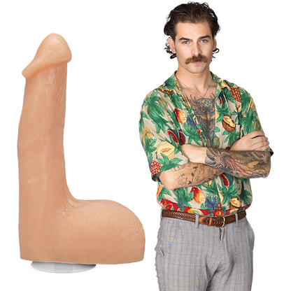 The Flesh Mechanic porn star stands fully clothed in 70's clothing with a bulge in their pants. The Signature Cocks - The Flesh Mechanic dildo is shown next to them, lifecast after their own shaft. | Kinkly Shop