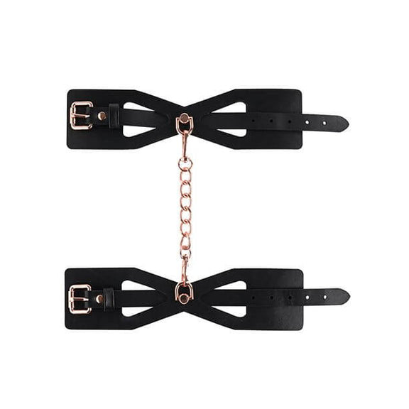 A top-down, lay flat image of the Sportsheets Brat Cuffs and their chain. The two cuffs are laid out flat, and the included chain is shown connecting the two D-rings together. The spot with the D-ring connector is the slimmest part of the cuff with the rest of the cuff at a thicker, wider size. | Kinkly Shop