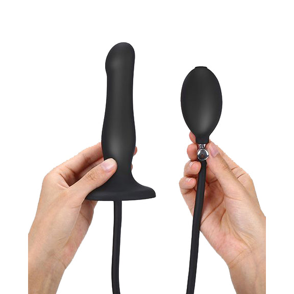 Two hands show the Strap-on-Me Inflatable Dildo Plug against a white background. One hand is holding the plug dildo itself while the other hand is holding up the inflatable bulb with quick-release valve. | Kinkly Shop