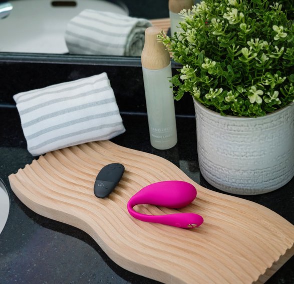 The We-Vibe Jive 2 shown on a bathroom countertop. It's sitting out next to a black palm-sized remote control that can control the vibrator. | Kinkly Shop