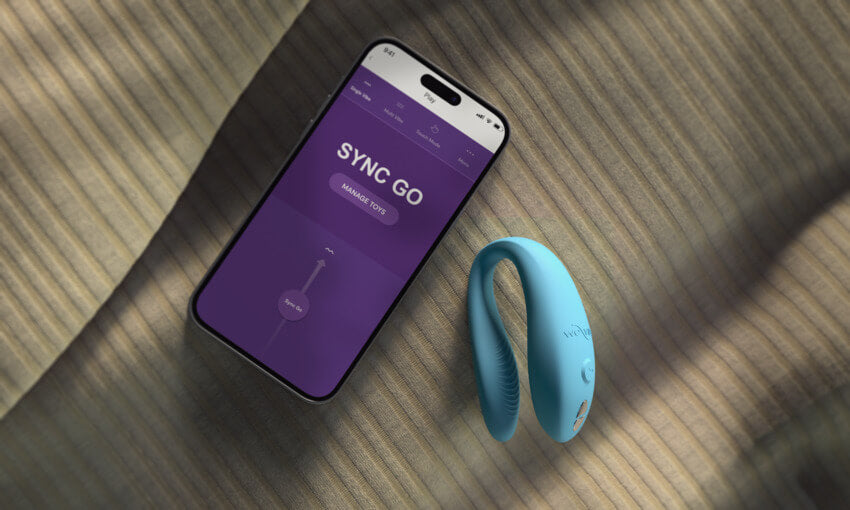 The We-Vibe Sync Go lays out next to a cell phone with the app showcased on it. The app is showing how the Sync Go's vibrations can be controlled by the app. | Kinkly Shop