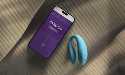 The We-Vibe Sync Go lays out next to a cell phone with the app showcased on it. The app is showing how the Sync Go's vibrations can be controlled by the app. | Kinkly Shop
