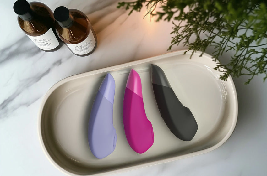 All three Womanizer Enhance vibrators laying out on a ceramic dish, letting the viewer see the difference between all three colors. | Kinkly Shop