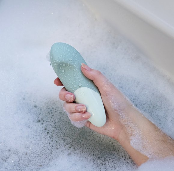 A person holds the Womanizer Vibe. It's covered in water droplets in the soapy bath. It looks like a comfortable grasp. | Kinkly Shop