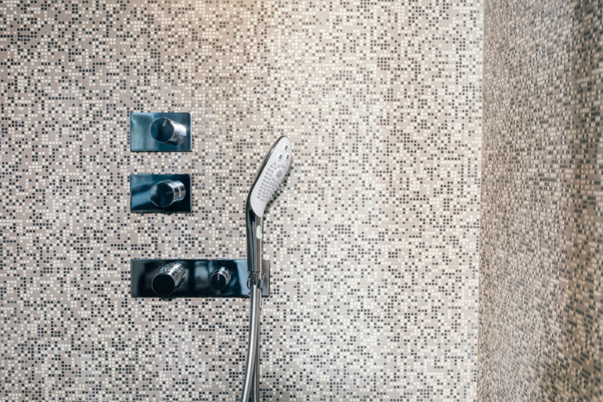 The Womanizer Wave shown installed in a heavily-tiled, fancy, spacious shower. It looks like a luxury shower head that fits in within the design of the shower. | Kinkly Shop