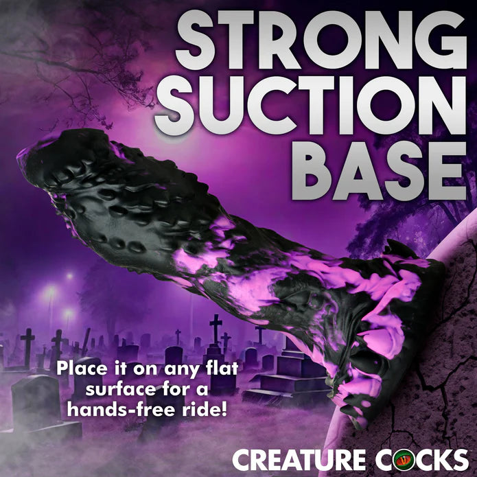 The Creature Cocks Grim shown with its base suction cupped onto a rock. Text on the image reads: "Strong suction base. Place it on any flat surface for a hands-free ride" | Kinkly Shop