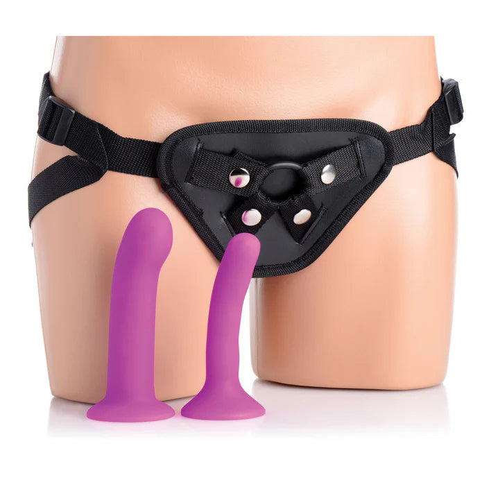 The Double G Vibrating Strap-On Kit shown with everything it comes with. The two included dildos are resting in front of a mannequin wearing a strap-on harness. | Kinkly Shop