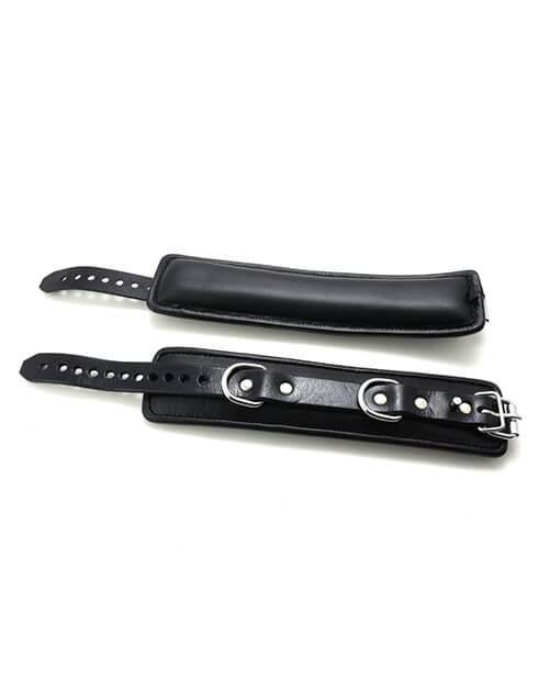 665 Padded Locking Wrist Restraints in black laid out flat. This allows you to see the thick, fluffy padded interior of the cuffs as well as the double D-rings built into the cuffs. | Kinkly Shop