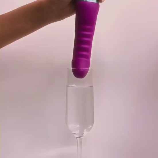 GIF shows a hand holding the tip of the FemmeFunn Cadenza in a glass of water. As the FemmeFunn Cadenza's intensity level is turned up, the water splashes out of the glass and all over the place. | Kinkly Shop
