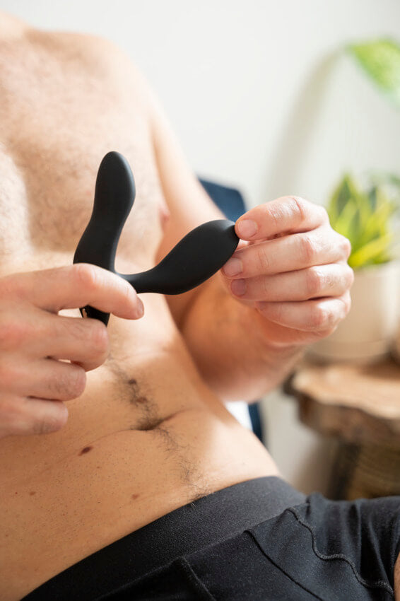 A person lounging in their underwear in front of their plants is holding the We-Vibe Vector+ in their hands. The tip of the We-Vibe Vector+ looks skinnier than two of the person's fingers. | Kinkly Shop