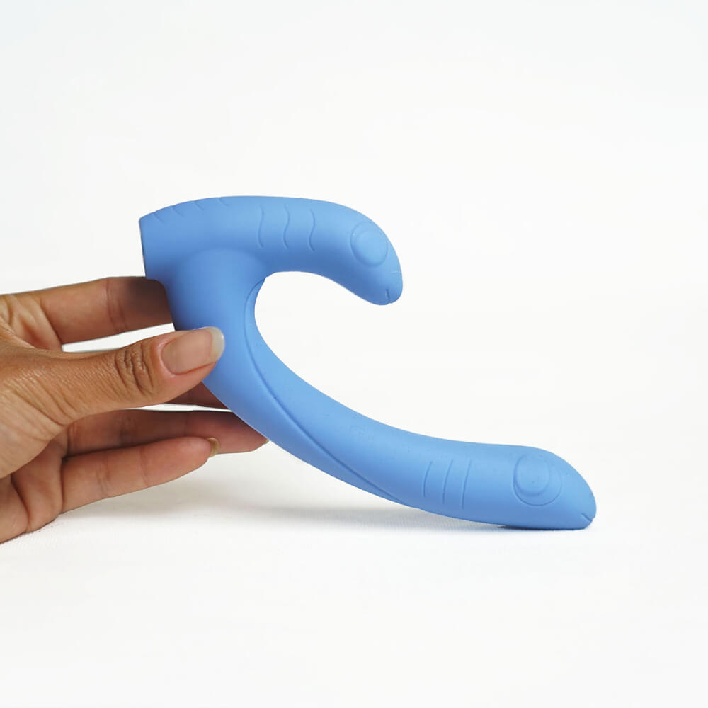 A person's hand props up the Cute Little Fuckers Jix against a plain white background. This well-lit surface showcases the two "faces" embedded into the surface of both points of the vibe. It also showcases the upward curvature of the shaft which can make it a great fit for g-spot and p-spot stimulation. | Kinkly Shop