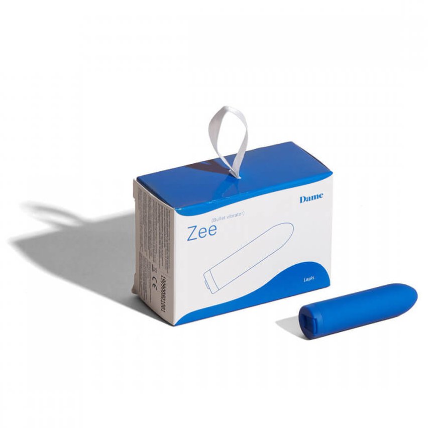 The Dame Zee micro bullet vibrator rests in front of the packaging for the Dame Zee micro bullet vibrator. | Kinkly Shop
