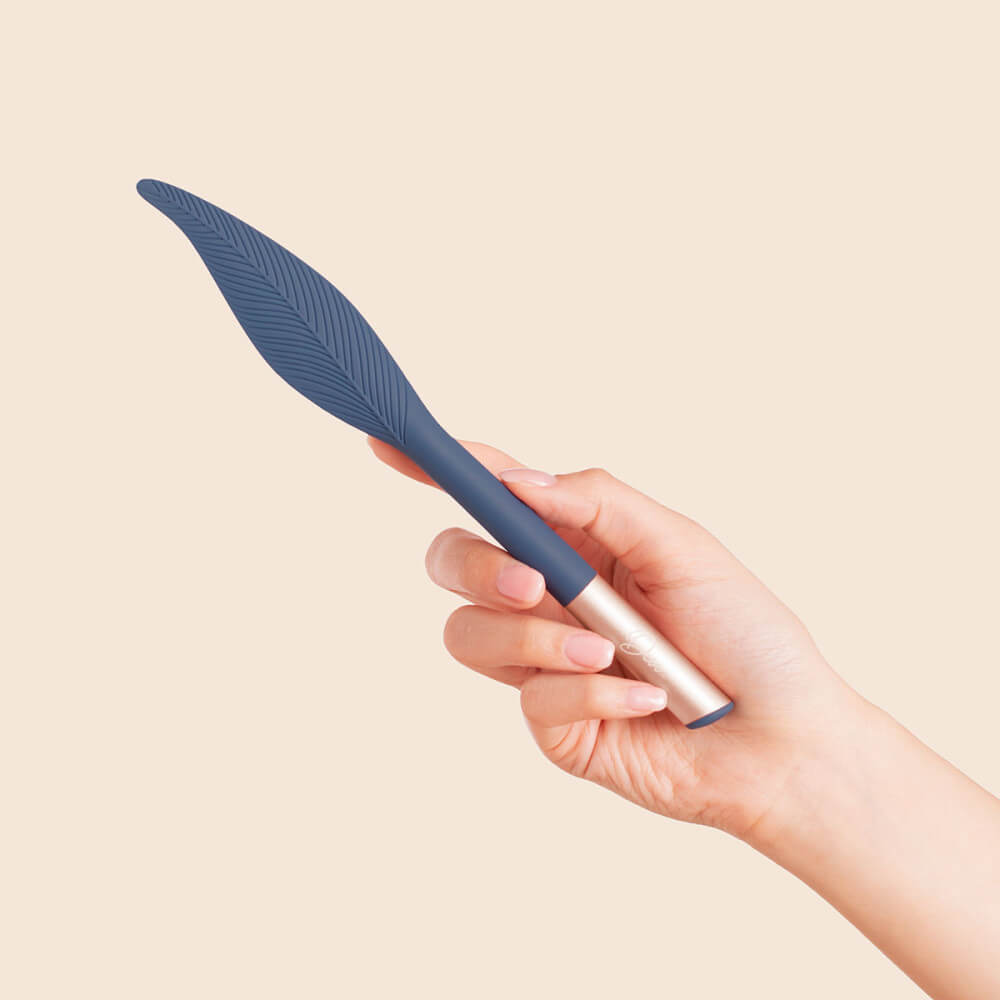 A hand holds the Deia Feather vibrator. The vibrator is clearly much longer than the person's hand - though the "feather" area is only about the length of the person's palm. The handle is extremely slim and looks smaller in width than a finger. | Kinkly Shop