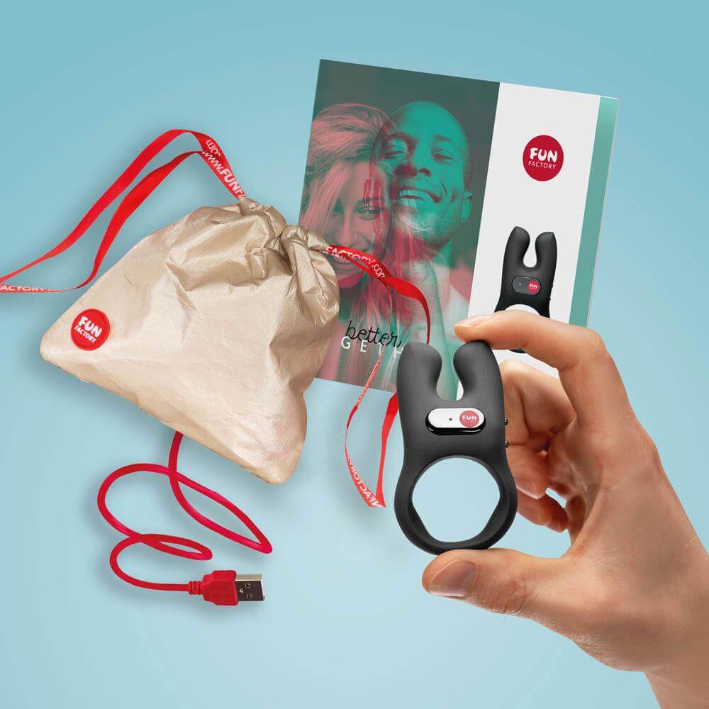 A person holds the Fun Factory NŌS in front of the rest of the items that come with the Fun Factory NŌS including the magnetic charging cable, the full-color instruction manual, and the high-quality drawstring sex toy storage bag. | Kinkly Shop