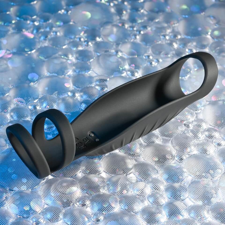 The Gender X Rocketeer laying against a unique, bubbled, textured background. This upscale view really showcases the three loop design (two at the base near the testicles with one near the head) as well as the magnetic charging port that rests within the interior chamber of the Gender X Rocketeer. | Kinkly Shop