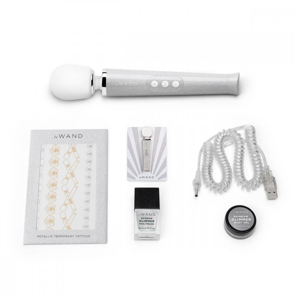 The White Le Wand All That Glimmers Wand Massager laid out next to everything that comes with the petite wand massager. That includes the color-coded charging cable, a glittery body gel, a matching enamel pin, a glittery nail polish, and a set of color-matching metallic temporary tattoos. | Kinkly Shop