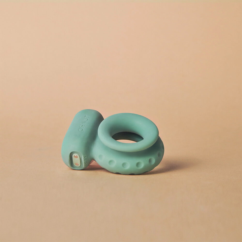 The OhNut Vibrating Ring laying on a brown surface. This side angle showcases the two magnetic ports on one side of the vibrator that allows for magnetic charging of the vibrator after each use. | Kinkly Shop