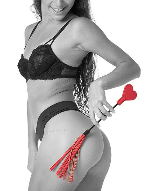 A person in lingerie holds the Sportsheets Amor Crop up against their butt. The tails of the flogger end droop slightly. The Sportsheets Amor Crop looks short and portable. | Kinkly Shop