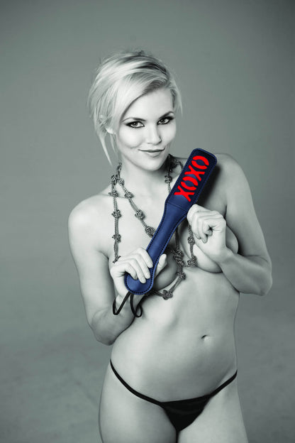 A person smiling while they hold the Sportsheets Black Vinyl Paddle, XOXO slapper in front of their body. | Kinkly Shop
