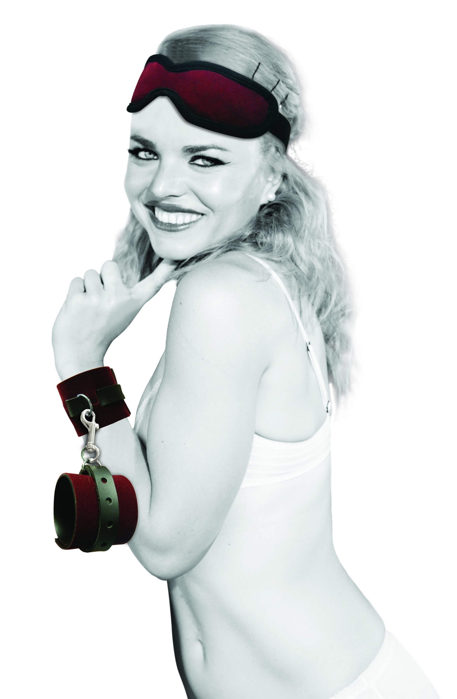 A happy, smiling person looks at the camera. The blindfold from the Sportsheets Enchanted Kit is resting on top of their head. One of the wrist restraints from the Sportsheets Enchanted Kit is on their wrist while the second restraint dangles from the one that's fastened on their wrist. | Kinkly Shop