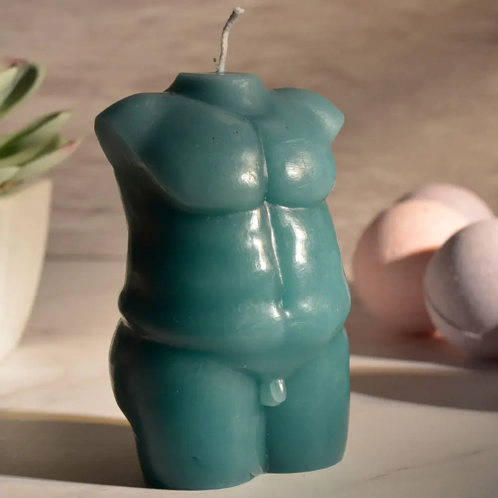 The Sportsheets Torso 2 Wax Play Candle sitting on top of a marbled countertop. There's mood lighting, and the image is very shadowed and moody. | Kinkly Shop