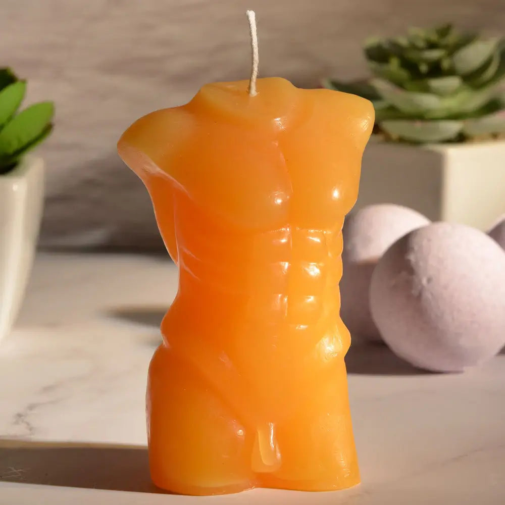 The Sportsheets Torso 4 Wax Play Candle sitting out on a marbled countertop with the deep afternoon sun casting long, dark shadows across the counter. | Kinkly Shop