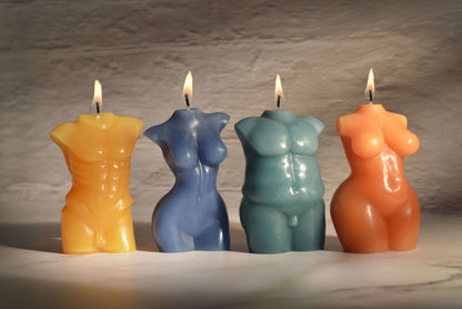 All of the four Sportsheets Torso Form Wax Play Candles sitting next to one another on top of a marbled surface. There's dark, moody lighting, and all of the candles are lit. This showcases all of the sculpted details of each candle. | Kinkly Shop