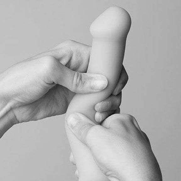 Two hands are squishy a Strap-on-Me Bendable Dual-Density Dildo. It shows how squishy the plushy material of the Strap-on-Me Bendable Dual-Density Dildo is. | Kinkly Shop