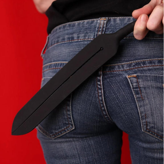 A person holds the Tantus Tawse Small up against their butt covered in jeans. The Tawse's size covers most of both butt cheeks, but this person appears to wear a very small jeans size. The handle fits easily into their hand. | Kinkly Shop