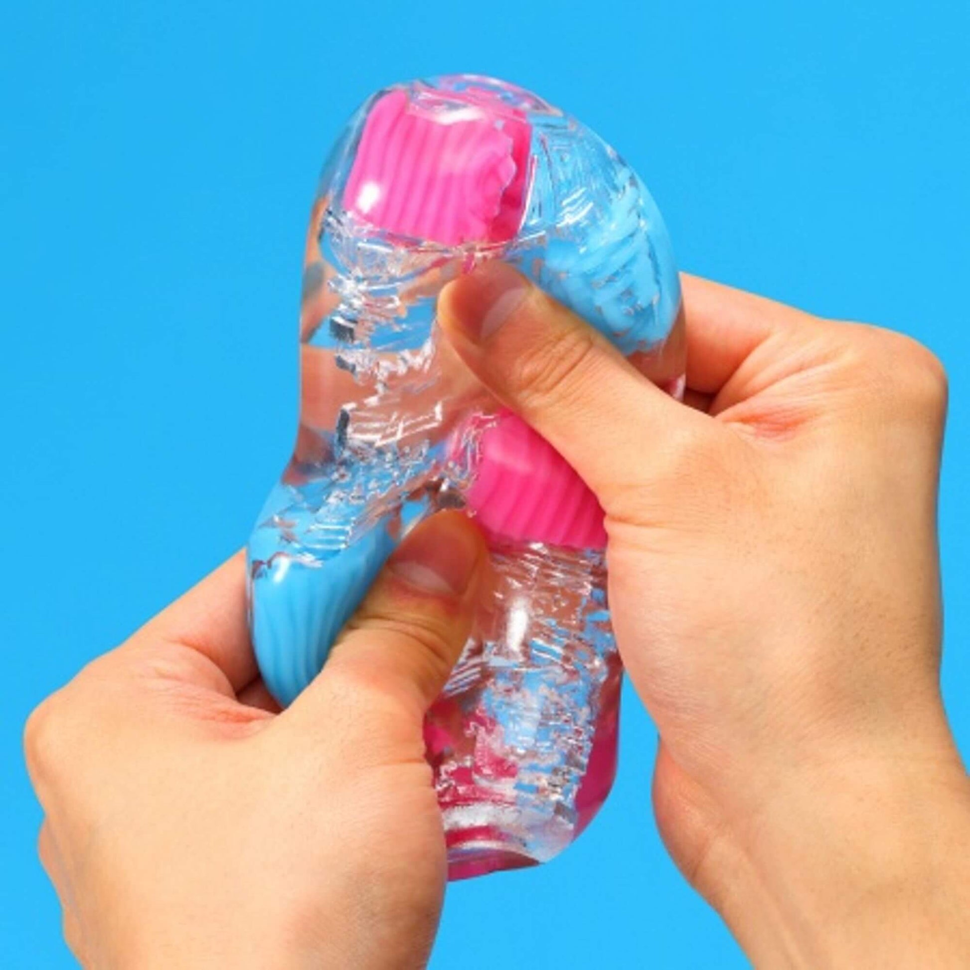 Two hands are gripping the Tenga Bobble, squishing it in different areas, showcasing the firm nodules that stand out from the softer, clear material. | Kinkly Shop