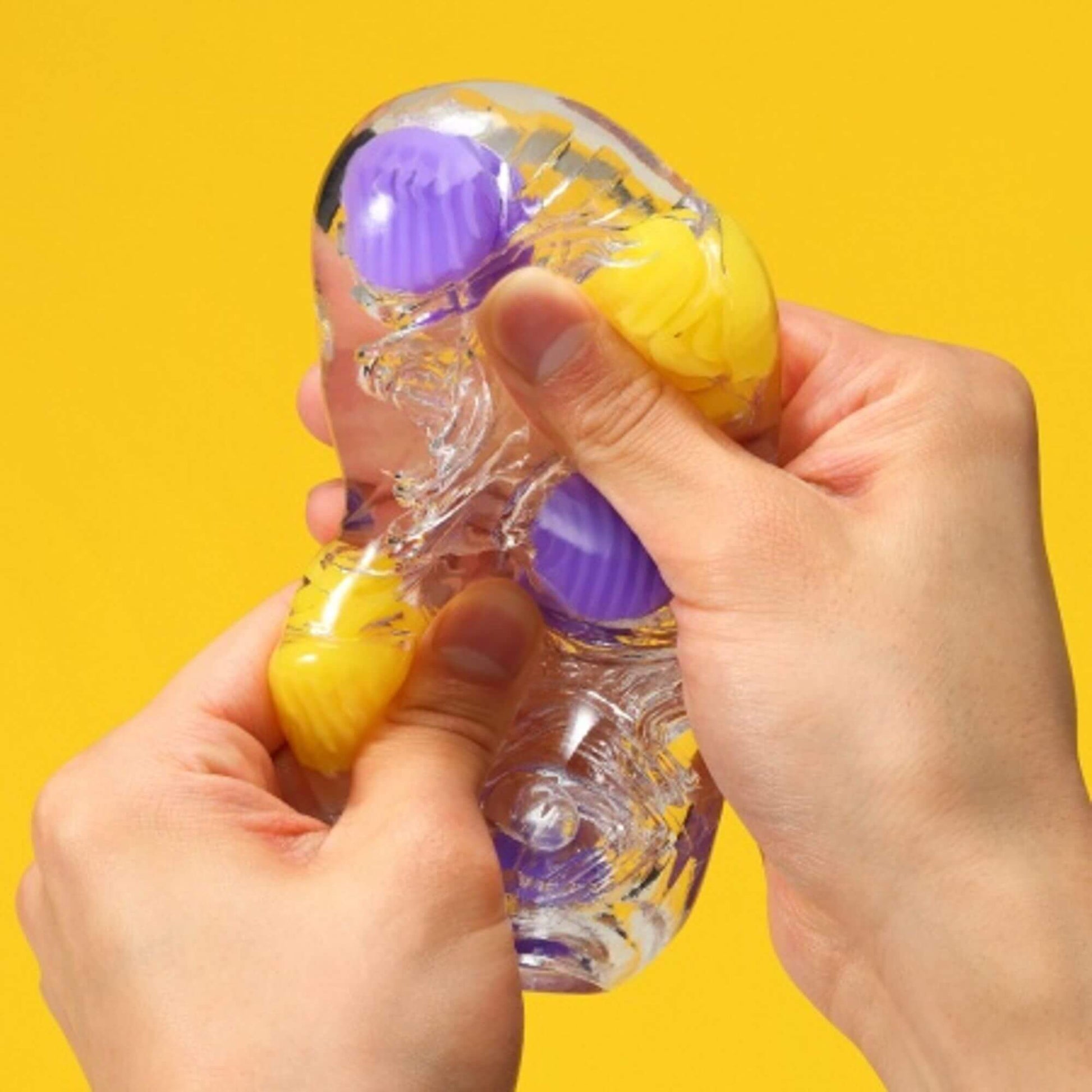 Two hands are gripping the Tenga Bobble, squishing it in different areas, showcasing the firm nodules that stand out from the softer, clear material. | Kinkly Shop