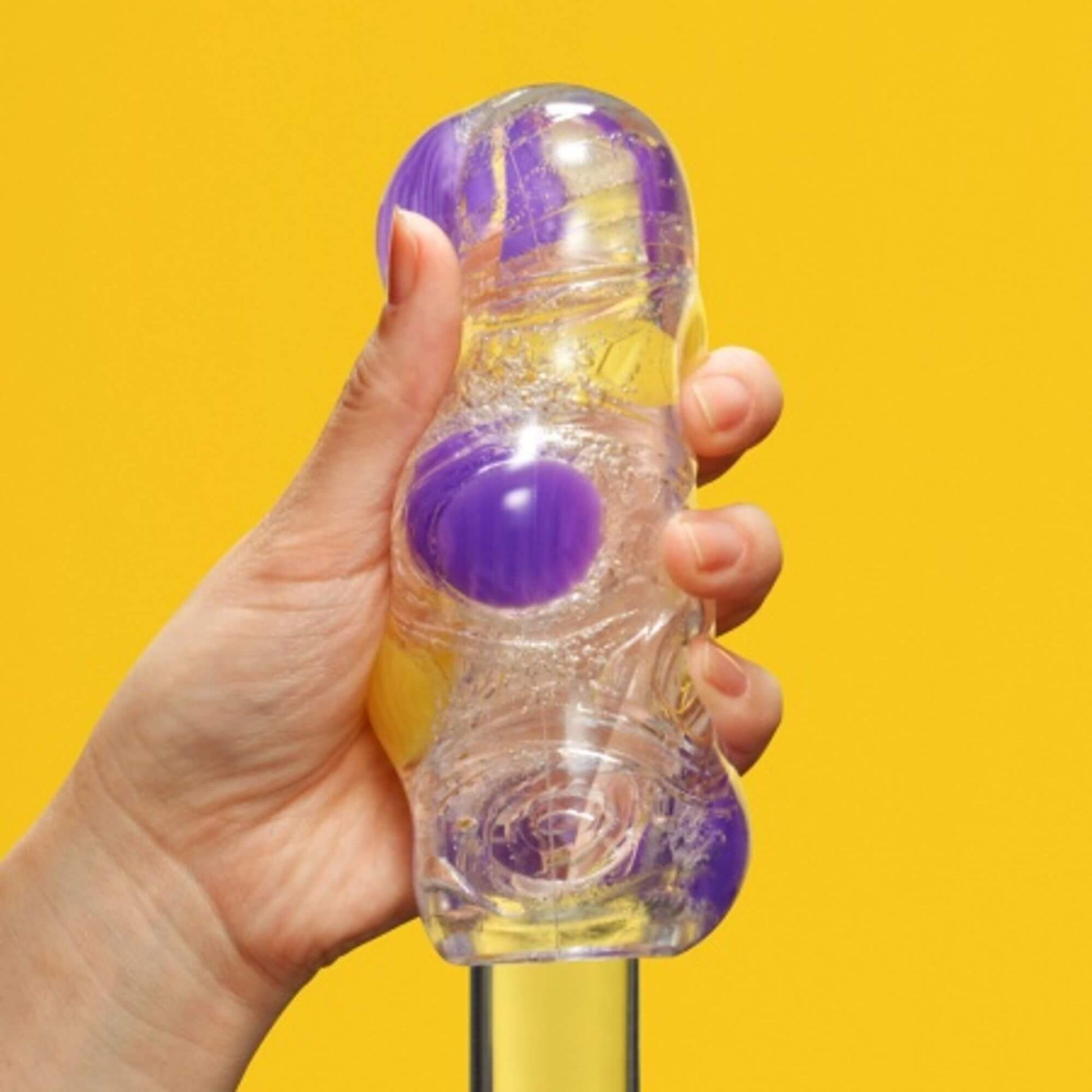 A hand holds the Tenga Bobble while the toy is being slid onto a clear, see-through glass dildo. The nodules visibly protrude away from the glass dildo to showcase the different textures. | Kinkly Shop