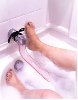 The Waterslyde Bathtub Water Diverter tied onto the water spout. A person's two feet are shown pressed against the shower wall while the Waterslyde Bathtub Water Diverter causes the water to flow between the person's legs. | Kinkly Shop
