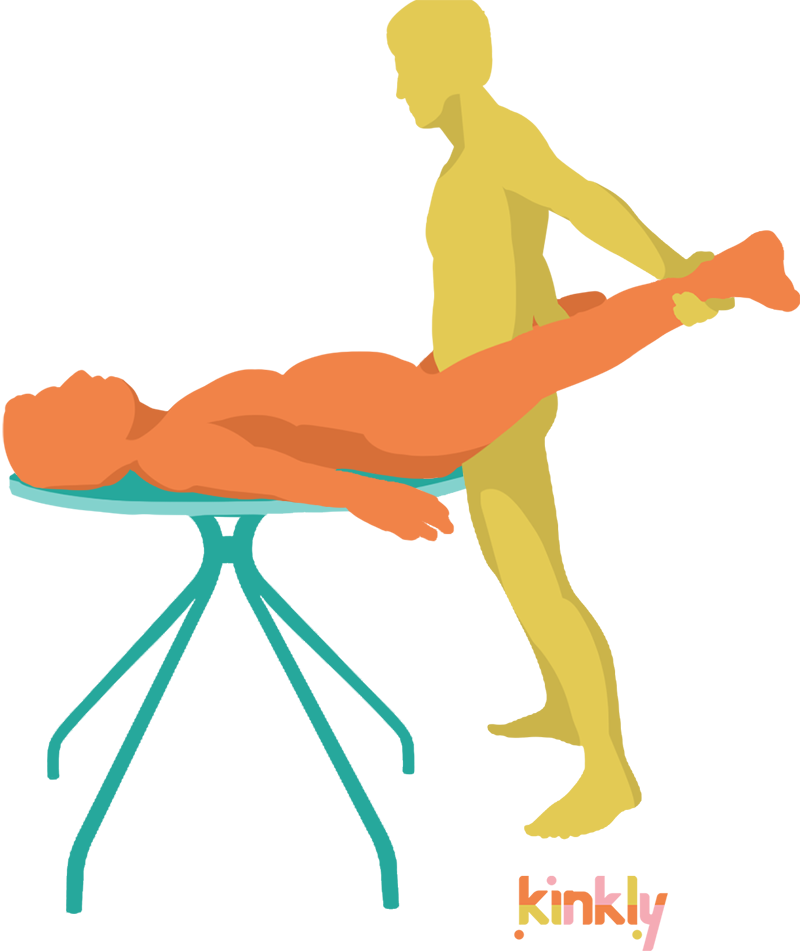 The receiving partner is laying flat on top of a supportive table. The penetrating partner spreads the legs and holds onto the ankles as they slide inside of their laying partner.