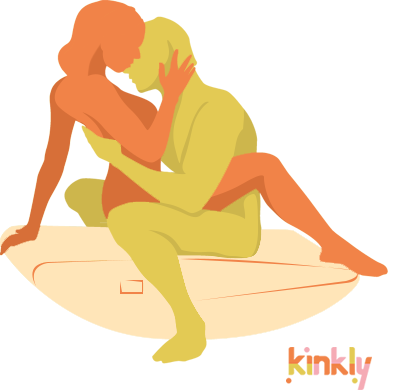 The Teeter Totter sex position. The penetrating partner is seated in the middle of the Scoop Rocker, straddling the shape with both feet flat on the floor on both sides of it. The receiving partner is seated in their lap, leaned back towards one end of the shape while their feet rest on the opposite end of the shape. | Kinkly