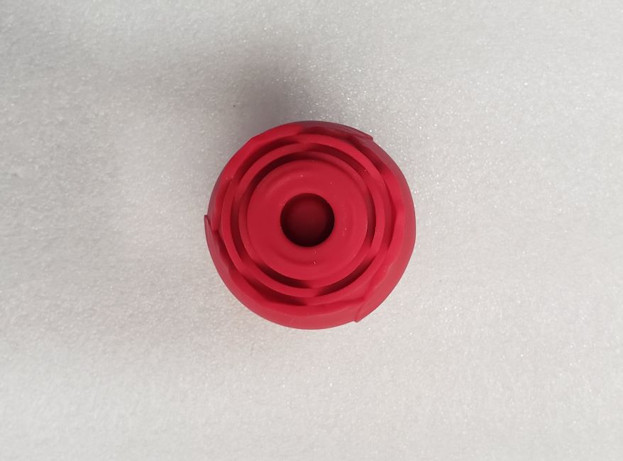 Rose Toy Vibrator: A bird's-eye shot of the Rose Suction Stimulator on a gray background. The toy is round and red with silicone petals like those of a rose.