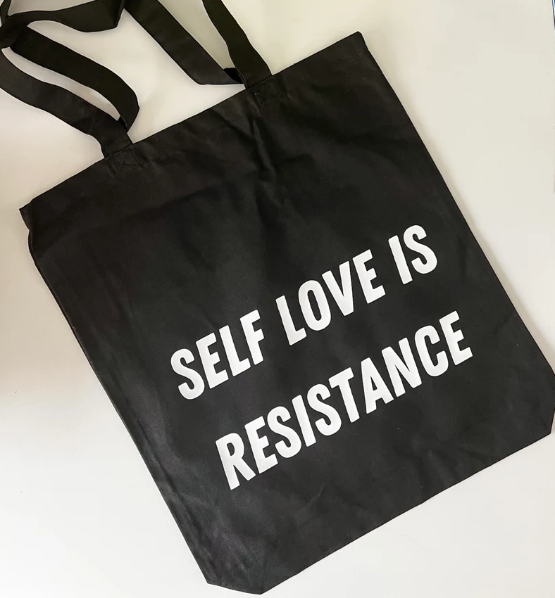 Black tote bag with white text that reads Self Love Is Resistance