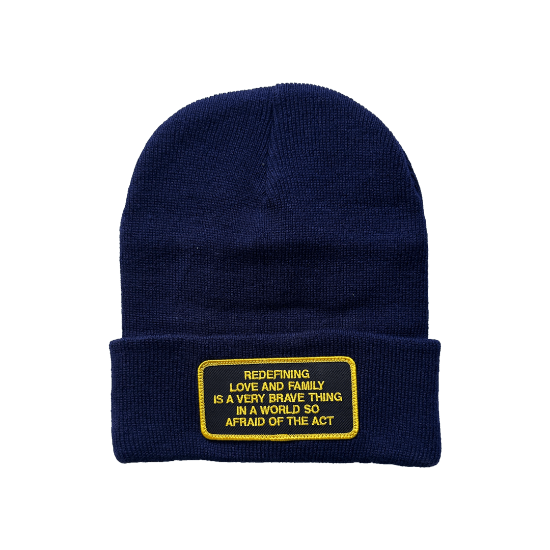 A navy beanie with a patch that reads: Redefining love and family is a very brave thing to do in a world so afraid of the act.