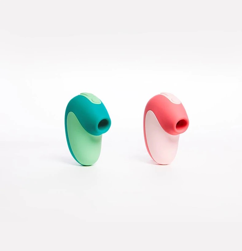 The Unbound Puff: Two matching suction vibrators in unique colour combinations next to each other. The vibrator on the left is teal and sea foam green and the vibrator on the right is baby pink and neon pink. Both vibrators are made up of a short, wide, curved handle with a downward-pointing circular suction cup for clitoral stimulation.