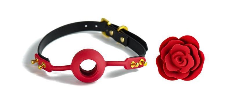 The ZALO Rose Ball Gag: A red ball gag with a large hole in the middle is attached to a black leather strap with a gold buckle and rounded gold duds. Next to the ball gag is a red rose-shaped plug, which can be inserted into the ball gag's hole to further restrict breathing.