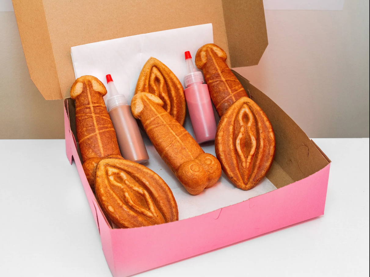 Box full of penis and vulva shaped waffles with two sauces, one pink, one brown