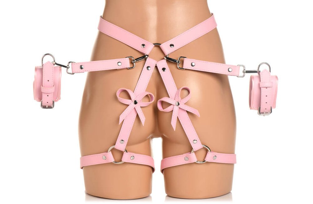 A mannequin wears the Strict Bondage Harness with Bows in pink. The optional cuffs are fastened onto the hip harness' O-ring as well. | Kinkly Shop